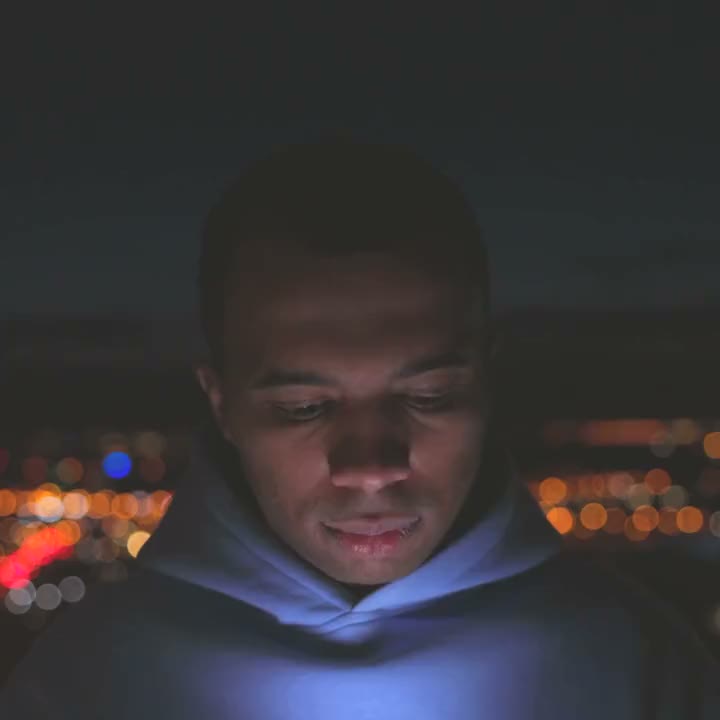 A man at night, his face lit by the phone in his hands.
